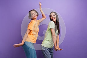 Photo of adorable pretty ladies wear t-shirts having fun dancing smiling isolated violet color background