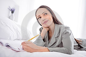 Photo of adorable pretty lady wear grey nightwear lying bed writing copybook indoors apartment bedroom