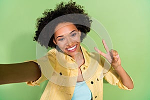 Photo of adorable pretty lady wear yellow denim jacket showing v-sign tacking selfie isolated green color background