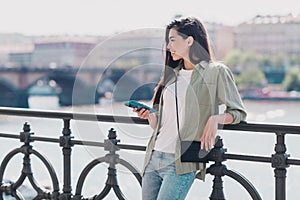 Photo of adorable sweet lady dressed casual clothes typing modern device enjoying sunshine outside urban embarkment