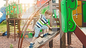 Photo of adorable toddler boy climbing and crawling on wooden staircase on children palyground at park