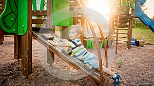 Photo of adorable toddler boy climbing and crawling on wooden staircase on children palyground at park