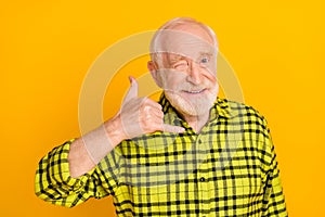 Photo of aged man happy positive smile show finger call phone sign wink eye isolated over yellow color background