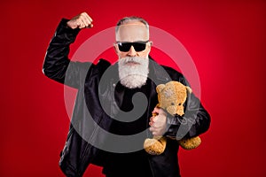 Photo of aged man serious confident ear eyeglasses hold hand strong protect teddy bear toy isolated over red color