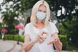 Photo of aged nice blond lady desinfect hands wear mask white t-shirt in park alone