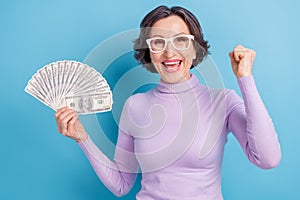 Photo of aged woman happy positive smile win money cash lottery lucky fists hands isolated over blue color background