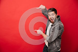 Photo of agitated man wih beard in casual clothing pointing fingers on copyspace text or product with surprise and smile, isolate