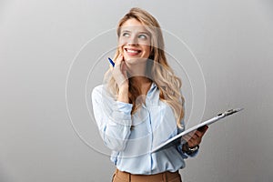 Photo of alluring blond secretary woman with long curly hair thinking and holding clipboard while working in office