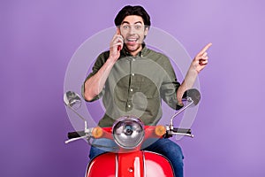 Photo of amazed brunette man point finger empty space talk phone wear jeans isolated on violet color background