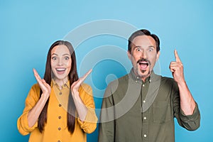 Photo of amazed cheerful mature man and woman point finger empty space sale isolated on blue color background
