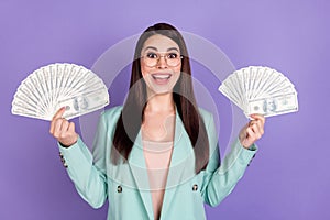 Photo of amazed cheerful young woman hold hands money cash good mood isolated on violet color background