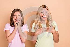 Photo of amazed mother and daughter hold hands chest cheeks news sale isolated on beige color background