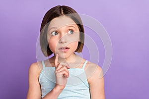 Photo of amazed shocked minded young little girl look empty space finger chin isolated on violet color background