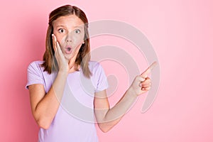 Photo of amazed shocked small girl hold hand cheekbone point finger empty space isolated on pink color background photo