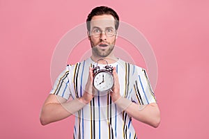 Photo of amazed shocked young man hold hands alarm clock late isolated on pastel pink color background