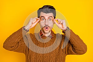 Photo of amazed young guy hold eyewear open mouth wear brown sweater isolated vibrant yellow background
