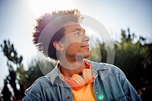 Photo of ambitious optimistic youngster dressed jeans jacket with headphones on neck posing in sunny weather look far in