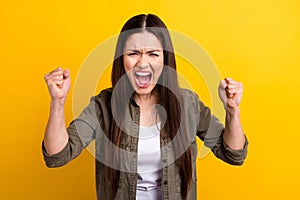 Photo of angry furious crazy young woman raise fists scream bad mood isolated on yellow color background