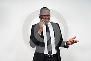 Closeup of angry young african man screaming while talking on smartphone over grey background