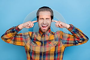 Photo of annoyed upset young man wear plaid shirt closed eyes fingers close ears isolated blue color background