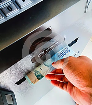 photo of an asian man's hand withdrawing Indonesian rupiah cash from an ATM machine