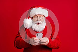 Photo of astonished old man in santa claus use smartphone read x-mas miracle ads discounts stare stupor wear sweater