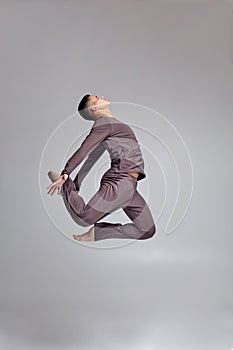 Photo of an athletic man ballet dancer dressed in a gray tracksuit, making a dance element against a gray background in