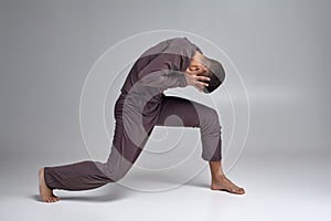 Photo of an athletic man ballet dancer dressed in a gray tracksuit, making a dance element against a gray background in