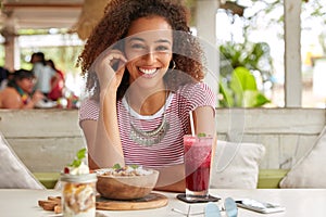 Photo of attractive black woman has Afro hairstyle, dressed in casual t shirt, smiles broadly at camera, rejoices