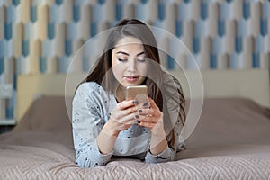 Photo of attractive concentrated woman holds mobile phone, sends messages to friend, downloads music files, connected to high