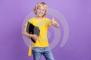 Photo of attractive cute school boy wear yellow t-shirt glasses holding mortarboard showing thumb up isolated purple