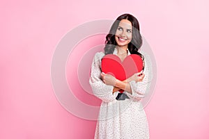 Photo of attractive dreamy young woman look empty space embrace red heart shape isolated on pastel pink color background