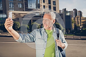 Photo of attractive handsome mature man dressed jeans shirt rucksack talking selfie modern device outside city srteet photo
