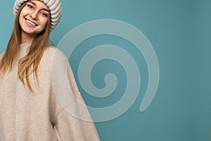 Photo of attractive happy smiling young dark blond woman isolated over blue background wall wearing beige warm sweater