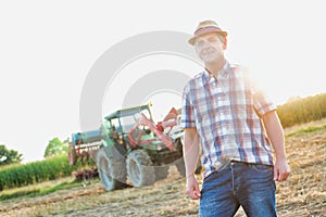 Attractive mature senior farmer standing against tractor in field photo