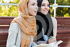 Photo of attractive muslim girls wearing headscarfs sitting in green park