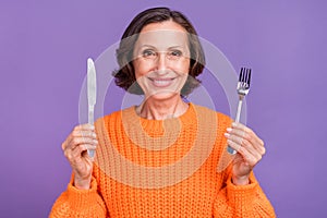 Photo of attractive senior woman hold metal cutlery ready to eat starving isolated over purple color background