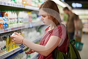 Photo of attractive young female consumer model with bobbed hairstyle, dressed in casual t shirt, stands in big store, holds bottl