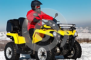 Photo of attractive young man in red warm winter clothes and black helmet on the ATV 4wd quad bike stand in heavy snow