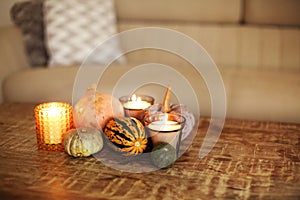 Photo of autumn decoration set of pumpkins and burning candles on wooden coffee table in living room