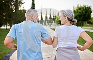 Photo from back of active mature couple smiling while jogging together in park in morning