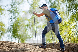 Photo from back of man with backpack and walking sticks on hill