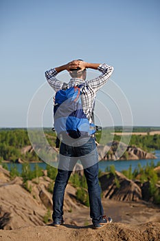 Photo back of tourist man with backpack with hands behind head on hill against backdrop of mountain expanses, blue sky