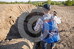 Photo from back of tourist man in cap with walking sticks at mountain canyon