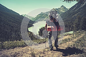 Photo from back of tourist man in cap with walking sticks on mountain hill near lake. tourist holding sticks