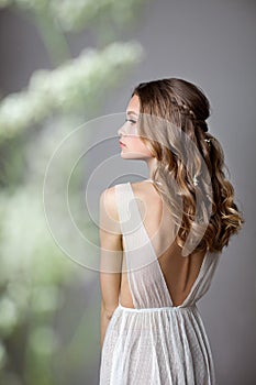 Photo from the back of a very beautiful young model in bridal dress with gypsophila flowers in her hands. Romantic style