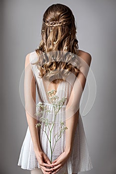 Photo from the back of a very beautiful young model in white dress with gypsophila flowers in her hands. Romantic style.