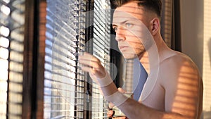 Photo of a bare-chested man peering out of a window