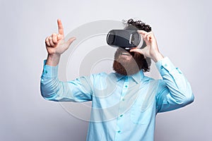 Photo of bearded man in blue shirt wearing VR glasses and touchi