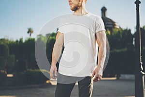 Photo Bearded Muscular Man Wearing White Blank t-shirt. Green City Garden Background at sunset. Horizontal Mockup